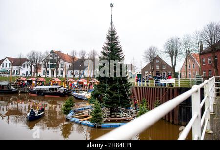 Carolinensiel, Deutschland. 27th. November 2021. Der schwimmende Weihnachtsbaum wird von Freiwilligen im Hafen des Dorfes aufgestellt. Seit 1995 wird der Baum traditionell am Samstag vor dem ersten Adventssonntag aufgesetzt und die Lichter eingeschaltet. Quelle: Hauke-Christian Dittrich/dpa/Alamy Live News Stockfoto