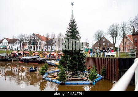 Carolinensiel, Deutschland. 27th. November 2021. Der schwimmende Weihnachtsbaum wird von Freiwilligen im Hafen des Dorfes aufgestellt. Seit 1995 wird der Baum traditionell am Samstag vor dem ersten Adventssonntag aufgesetzt und die Lichter eingeschaltet. Quelle: Hauke-Christian Dittrich/dpa/Alamy Live News Stockfoto