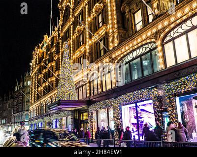 HARRODS CHRISTMAS SHOPPING Einkaufen Londoner Kaufhaus Harrods in der Dämmerung mit Weihnachtsbeleuchtung Menschenmengen und vorbeifahrende Autos Knightsbridge London SW1 Stockfoto