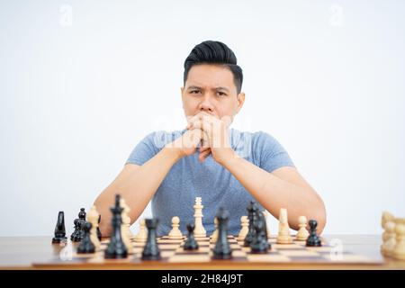 Junger Mann mit zwei Händen im Mund, während er Schach spielt Stockfoto