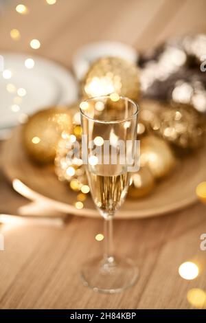 Weihnachtliche Tischdekoration mit goldenen Weihnachtsdekorationen. Neujahrsfest. Ein Glas Champagner Stockfoto