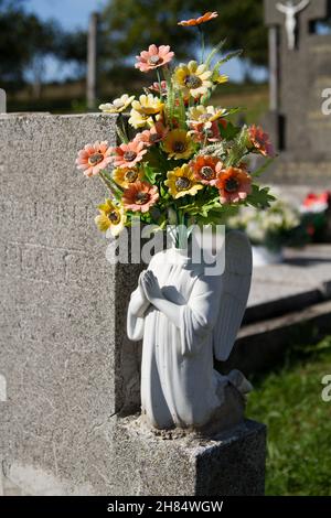 Eine beschädigte Statue eines Engels auf einem Grab, mit einem Strauß gefälschter Blumen anstelle des Kopfes. Slowakei. Stockfoto