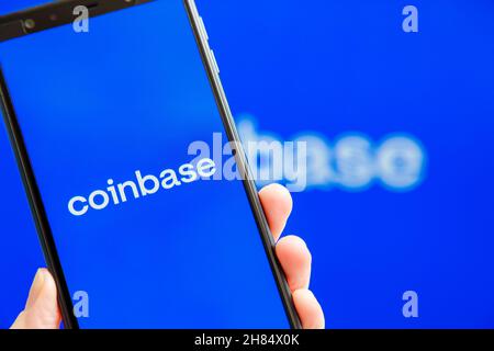 Ukraine, Odessa - Oktober, 9 2021: Hand hält Handy mit Coinbase App läuft auf dem Smartphone-Bildschirm mit Coinbase Logo im Hintergrund. Coinbase - Ame Stockfoto