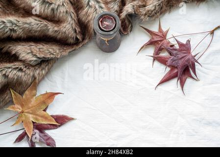 Herbst-Grußkarten-Mockup-Szene mit Ahornblättern, Duftkerze und Karo. Weiße Tischdecke Hintergrund.Draufsicht, flache Lage, Kopierraum Stockfoto