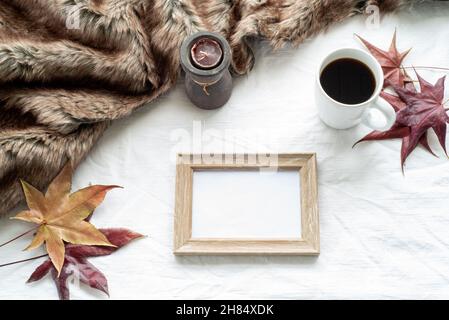 Herbstfrühstückszene. Leerer Bilderrahmen aus Holz mit Ahornblättern, einer Tasse Kaffee, Duftkerze und Plaid. Weißer Tischdecke Hintergrund. Bis Stockfoto