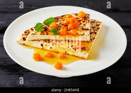 Leipajuusto, Kaffeost, Brotkäse, finnische Quietschscheiben mit Moltebeermarmelade und frischer Minze auf einem weißen Teller auf einem schwarzen Holztisch Stockfoto