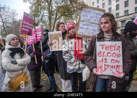 London, Großbritannien. 27th. November 2021. „Priti Patel Wie Schlafen Sie Nachts??? Safe Passage Now - F*ck the Tories' und 'Ihr Blut liegt auf deinen (Händen)' Postern. Ein Notfallprotest nach den jüngsten tragischen Ertrinken im Ärmelkanal, der Care4Calais aufgerufen wurde und sich gegen Rassismus einsteht, forderte sichere und legale Wege für Flüchtlinge, nach Großbritannien zu kommen. Das rassistisch-feindliche Umfeld der Regierung und der jüngste Angriff auf Flüchtlinge und Migranten im Gesetz über Nationalität und Grenzen hat und wird weiterhin zu dem Schrecken und der Tragödie des Verlusts von Menschenleben im Kanal führen und für eine sichere Passage für alle aufrufen Stockfoto