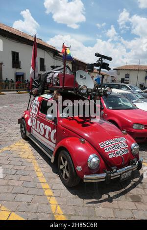 VW Käfer Volkswagen Mapping Straßen in Cusco Peru Wolken rotes Fahrzeug google Earth Maps Fahnen Schilder Straßenhäuser staubiges Wetter heiß Stockfoto