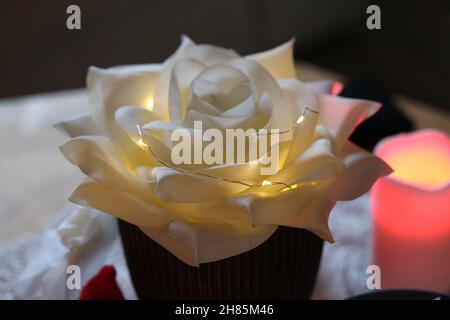 Große weiße gefälschte Blumendekorationen mit kleinen festlichen Weihnachtslichtern darin. Kerze im Hintergrund. Schönes, einzigartiges Nahaufnahme-Bild. Stockfoto