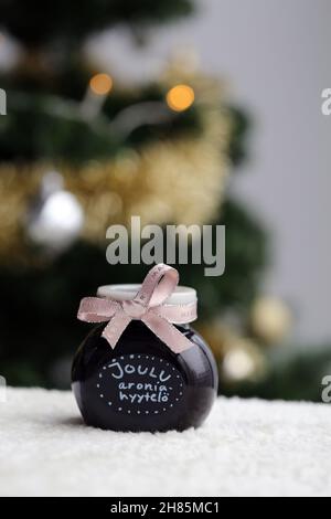 Hausgemachte weihnachtliche Marmelade in einem Glas mit hellroter Schleife. Apfelbeermarmelade im Inneren. Nahaufnahme des Farbbildes mit dem Baum im Hintergrund. Stockfoto