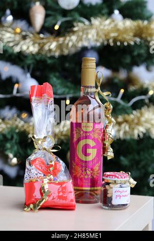 Luomu Rose Glögi - ein traditionelles organisch-alkoholisches finnisches Glogg-Getränk mit Lindt-Schokolade, Rosinen und Mandeln auf einem Tisch mit einem Weihnachtsbaum. Stockfoto