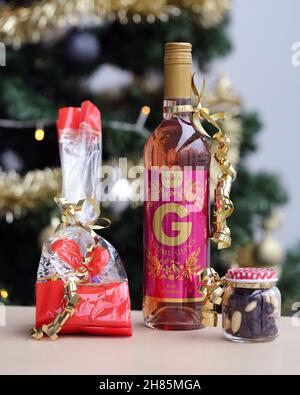 Luomu Rose Glögi - ein traditionelles organisch-alkoholisches finnisches Glogg-Getränk mit Lindt-Schokolade, Rosinen und Mandeln auf einem Tisch mit einem Weihnachtsbaum. Stockfoto