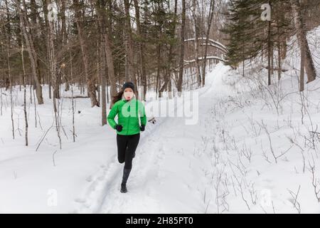 Laufsport Frau. Die Läuferin joggt im kalten Winterwald in warmer, sportlicher Laufkleidung und Handschuhen. Schöne Passform asiatisch kaukasischen Weibchen Stockfoto