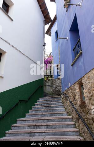 Schmale Straße mit bunten Häusern im malerischen Dorf Ribadesella, Asturien, Spanien, mit einer Treppe im Vordergrund, vertikal Stockfoto