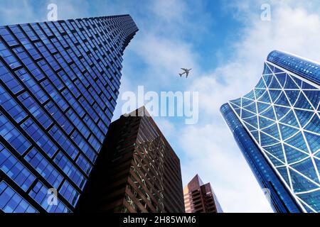 Blick von unten auf hohe Bürogebäude im Geschäftsviertel von Calgary vor einem blauen und bewölkten Himmel mit Flugzeug über dem Kopf. Stockfoto