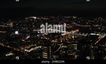 Panoramablick in der Nacht mit Stadtlichtern auf dunklem Himmel Hintergrund. Blick vom Bullauge aus auf eine große Stadt mit schönen Lichtern, Nachtleben-Konzept. Stockfoto