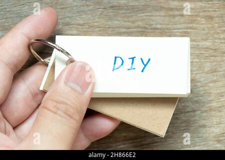 Mann hält die Flash-Karte mit dem handschriftlichen Wort DIY (Abkürzung für Do it yourself) auf Holzhintergrund Stockfoto