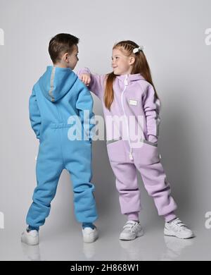 Zwei niedliche Kinder in blauen und rosa Jumpsuits stehen nebeneinander, Junge mit dem Rücken zu uns und Mädchen mit ihrem Gesicht Stockfoto