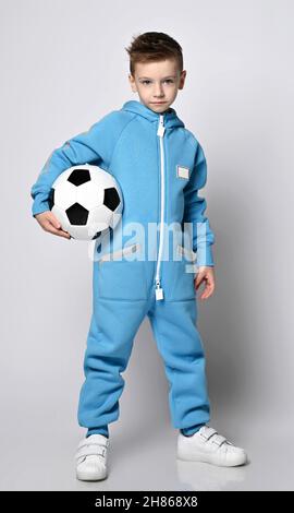 Frolic, Active Kid Boy in blauem Jumpsuit mit Kapuze und Taschen mit reflektierenden Streifen steht für den Fußball Stockfoto
