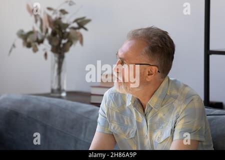 Nachdenklicher älterer Mann, der die Entscheidung trifft und zu Hause auf der Couch sitzt Stockfoto