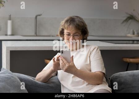 Fröhliche, fröhliche ältere Dame in einer Brille, die SMS liest Stockfoto