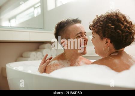 Unbeschwertes junges queeres Paar, das zu Hause ein romantisches Schaumbad hat. Glückliches junges Paar, das sich in der Badewanne amüsieren kann. Junge LGBTQ+-Paar Ausgaben Stockfoto