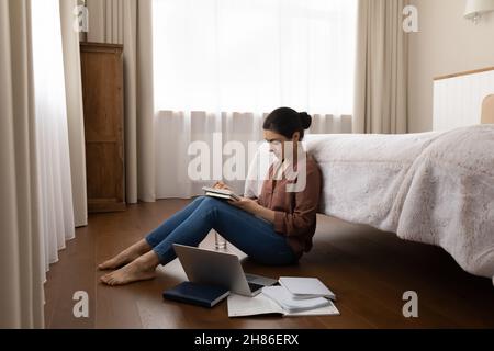 Glückliche junge inderin, die studiert und auf dem Boden sitzt. Stockfoto