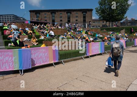 Menschenmassen auf der Canalside Green Steps, Kings Cross, london, gegenüber dem Breitbild-Fernseher, der tagsüber im Sommer Sport im Freien in der Nähe von Coal Drops Yard zeigt Stockfoto