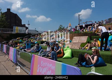 Menschenmassen auf der Canalside Green Steps, Kings Cross, london, gegenüber dem Breitbild-Fernseher, der tagsüber im Sommer Sport im Freien in der Nähe von Coal Drops Yard zeigt Stockfoto