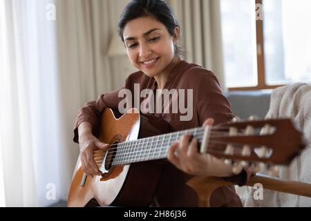 Lächelnde junge indische Frau, die zuhause Gitarre spielt. Stockfoto