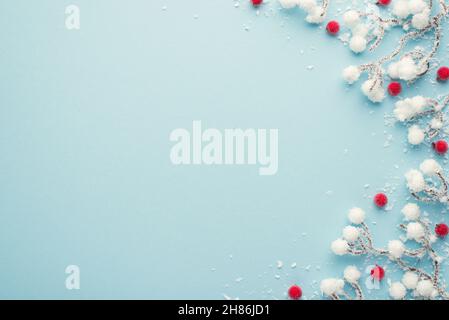 Draufsicht Foto von weihnachtsdekorationen Schnee Äste mit roten Stechbeeren auf isolierten pastellblauen Hintergrund mit leerem Raum Stockfoto