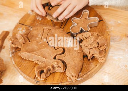 Kinderhände schnitzen Kekse auf Lebkuchenteig aus Figuren. Mädchen bereitet weihnachtskekse auf einem Holztisch zu Stockfoto