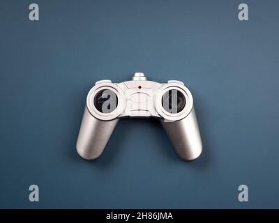 Silberne Funkfernbedienung im Retro-Stil für ein Spielzeug isoliert auf blauem Hintergrund, Draufsicht. Game Controller Joystick, flach liegend, minimalistischer Stil. Stockfoto