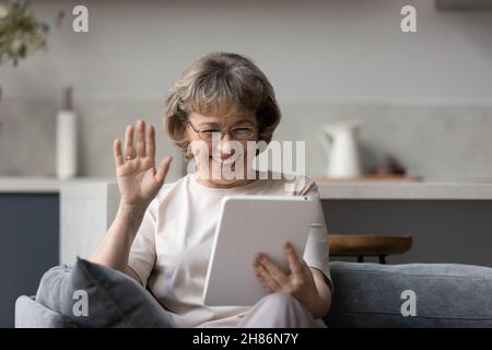 Glückliche reife 60s Frau winkende Hand hallo auf Tablet-Bildschirm Stockfoto