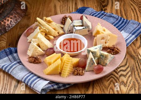 Käseplatte. Köstliche Käsemischung mit Walnüssen, Marmelade auf Holztisch. Leckere Vorspeise mit Käse für Wein. Stockfoto