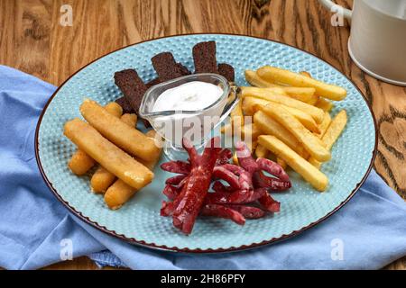 Biersnacks-Auswahl auf Holzhintergrund. Wurst, gegrillter Käse, Pommes Frites, Croutons und Creme-Knoblauch-Souse Stockfoto