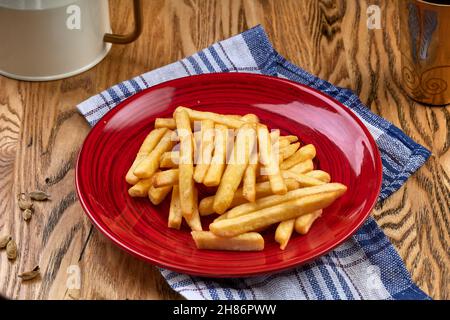 Pommes frites auf einem roten Teller, auf einem hölzernen Hintergrund Stockfoto