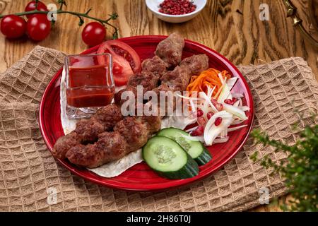 Leckerer lula Kebab auf dem Teller auf einem Holztisch. Gehacktes Fleisch auf Holzspießen, gegrillt. Östliche Küche. Stockfoto