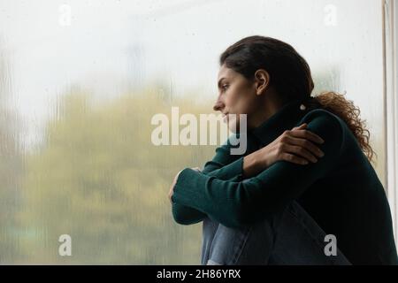 Einsame junge Latina-Hündin sitzt auf dem Fensterbrett und beobachtet draußen den Regen Stockfoto