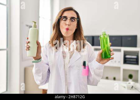 Junge Ärztin mit Aloe Vera und Creme, die Fische mit Mund und blinden Augen ins Gesicht macht, verrückt und komisch. Stockfoto