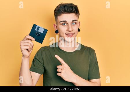 Junger kaukasischer Junge mit Ohren, die die Diskette mit lächelndem Lächeln und mit Hand und Finger zeigen Stockfoto