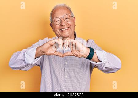 Älterer Mann mit grauen Haaren trägt elegantes Hemd und Brille lächelnd in der Liebe zeigt Herz-Symbol und Form mit den Händen. Romantisches Konzept. Stockfoto
