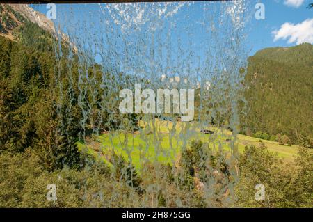 Tiroler Alpenlandschaft wie durch einen Vorhang aus Wasser hinter einem Wasserfall gesehen. Im Stubaital, Tirol, Österreich fotografiert. Stockfoto