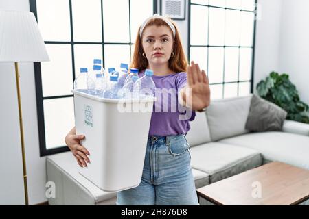 Junge Rotschopf Frau hält Recycling-Papierkorb mit Plastikflaschen tun aufhören zu singen mit Handfläche der Hand. Warnung Ausdruck mit Negativ und ser Stockfoto