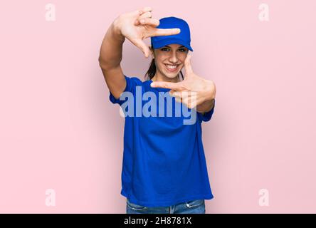 Junge hispanische Mädchen tragen Lieferung Kurier uniform lächelnd machen Rahmen mit Händen und Fingern mit glücklichem Gesicht. Kreativität und Fotografie Konzept. Stockfoto