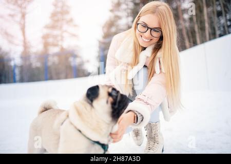 Junge Frau geht in den Wintersport auf Eislaufbahnen mit Mops Hund. Stockfoto