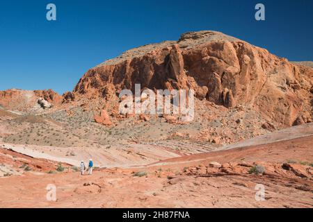 Valley of Fire State Park, Nevada, USA. Blick auf den Gibraltar Rock vom Fire Wave Trail aus, zwei Wanderer überqueren rote Sandsteinfelsen. Stockfoto