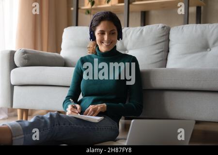 Lächelnde hispanische Dame mit Kopfhörern, die Weblektion am pc ansehen Stockfoto