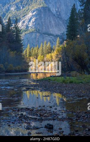 Yosemite-Nationalpark, Kalifornien, USA. Blick auf den ruhigen Merced River in der Nähe von Yosemite Village, herbstliche, hohe Granitklippen, die sich über dem Hotel erheben. Stockfoto