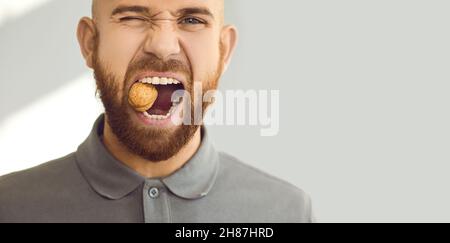 Kopfbild eines jungen Mannes mit gesunden Zähnen, der versucht, eine harte Walnuss zu knacken Stockfoto